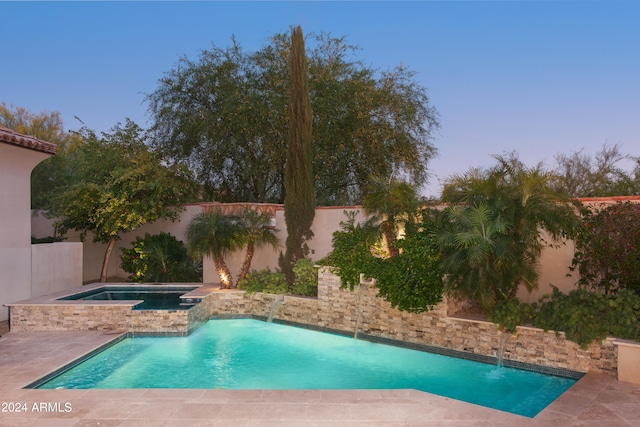 pool at dusk featuring a patio, an in ground hot tub, and pool water feature