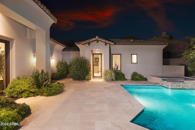 pool at night with a patio area and an in ground hot tub