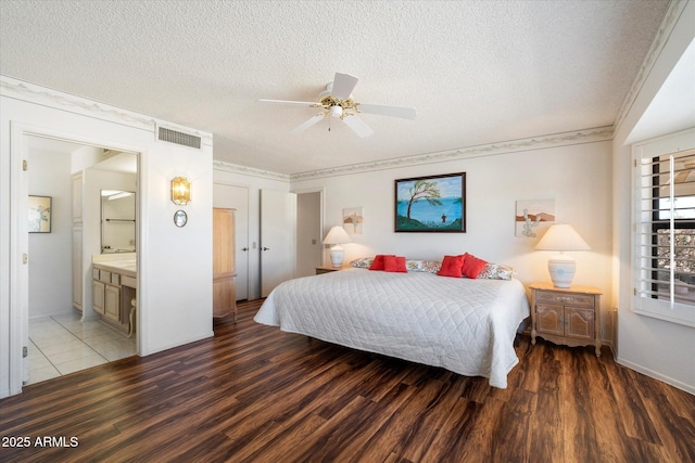 bedroom featuring connected bathroom, a textured ceiling, visible vents, and wood finished floors