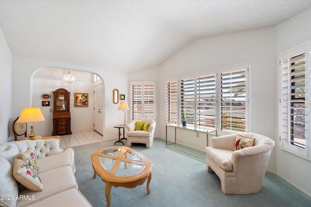 carpeted living area with arched walkways, vaulted ceiling, a textured ceiling, and an inviting chandelier