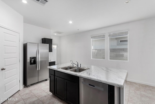 kitchen featuring light stone countertops, stainless steel appliances, sink, light tile patterned floors, and a center island with sink