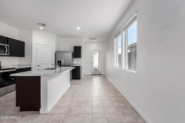 kitchen with light tile patterned floors, appliances with stainless steel finishes, sink, and an island with sink