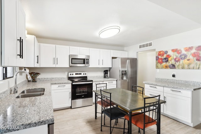 kitchen with sink, white cabinetry, light hardwood / wood-style flooring, appliances with stainless steel finishes, and light stone countertops