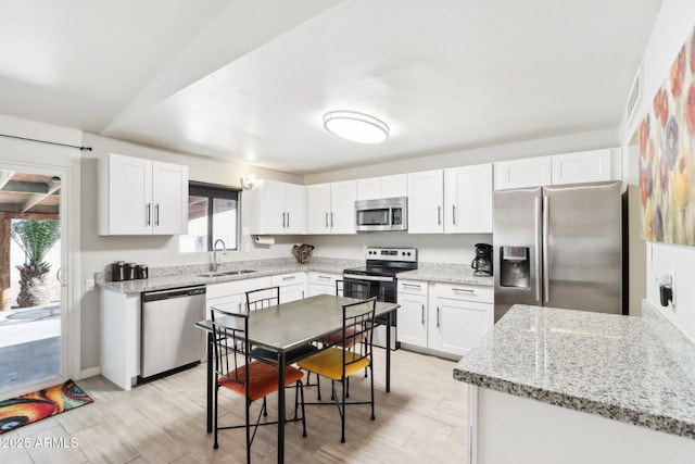 kitchen with sink, white cabinetry, light stone counters, stainless steel appliances, and light hardwood / wood-style floors