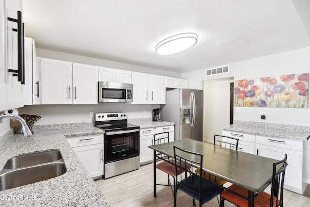 kitchen with white cabinetry, appliances with stainless steel finishes, light stone countertops, and sink