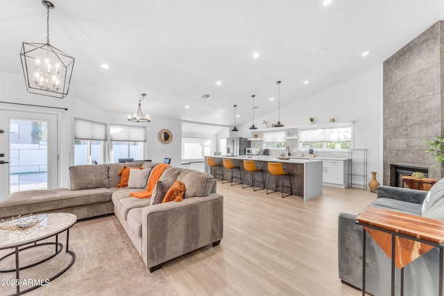 living room with high vaulted ceiling, a wealth of natural light, an inviting chandelier, and light hardwood / wood-style flooring