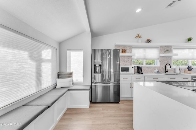 kitchen featuring sink, stainless steel fridge, a wealth of natural light, white cabinets, and vaulted ceiling