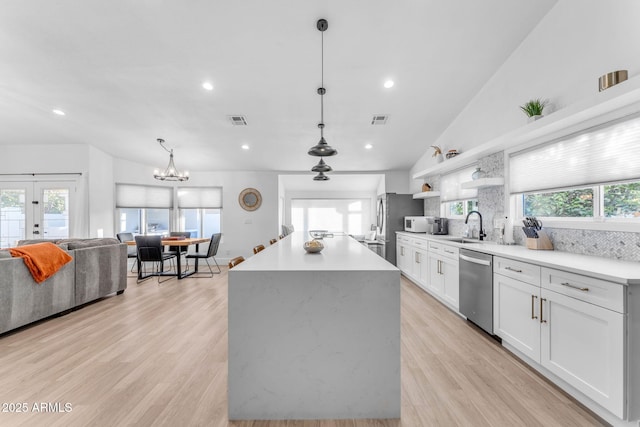 kitchen featuring white cabinetry, hanging light fixtures, dishwasher, a kitchen island, and decorative backsplash