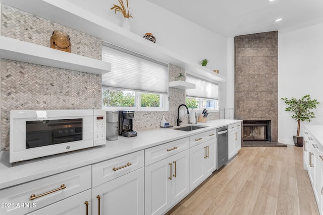 kitchen featuring a fireplace, white cabinetry, sink, backsplash, and light hardwood / wood-style floors