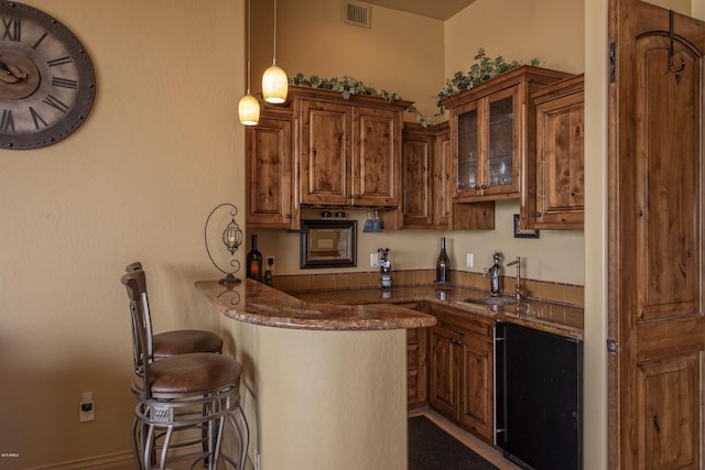 kitchen featuring pendant lighting, sink, dark stone countertops, a kitchen bar, and kitchen peninsula