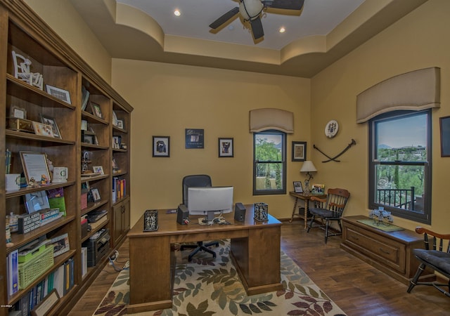 office area with a raised ceiling, ceiling fan, and dark wood-type flooring