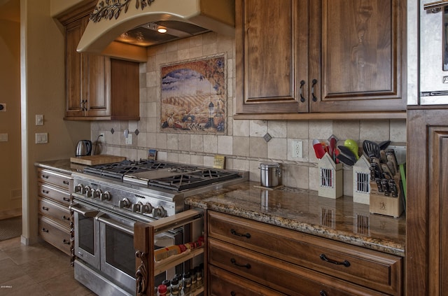 kitchen with double oven range, premium range hood, stone counters, tile patterned flooring, and decorative backsplash