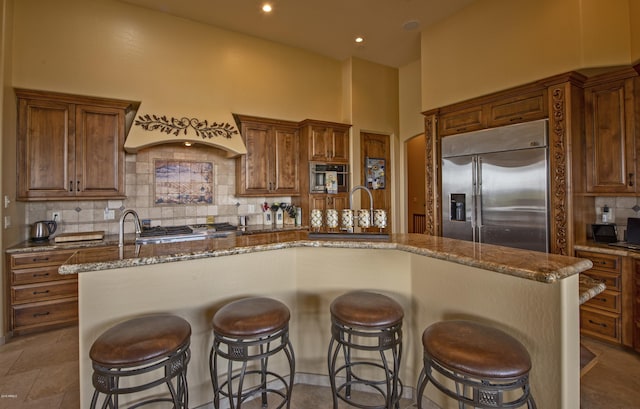 kitchen featuring decorative backsplash, a spacious island, sink, a high ceiling, and built in fridge