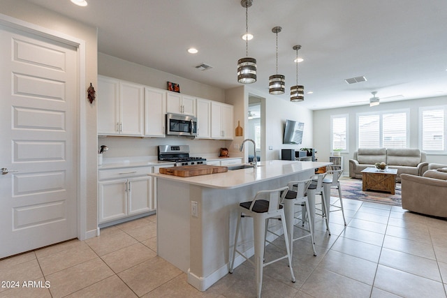 kitchen with hanging light fixtures, an island with sink, white cabinets, and appliances with stainless steel finishes