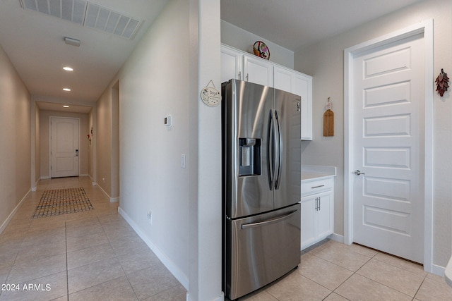 kitchen with light tile patterned flooring, stainless steel fridge, and white cabinetry