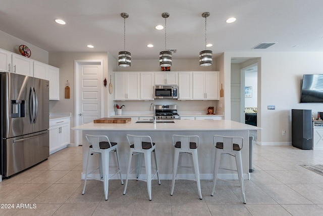 kitchen featuring a kitchen island with sink, white cabinetry, stainless steel appliances, and decorative light fixtures