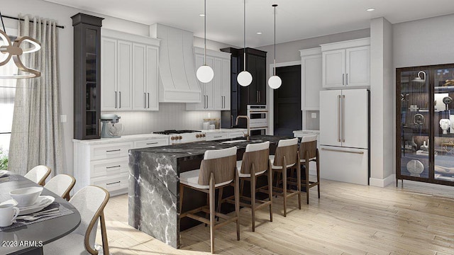 kitchen featuring a center island with sink, backsplash, premium range hood, light hardwood / wood-style flooring, and high end fridge