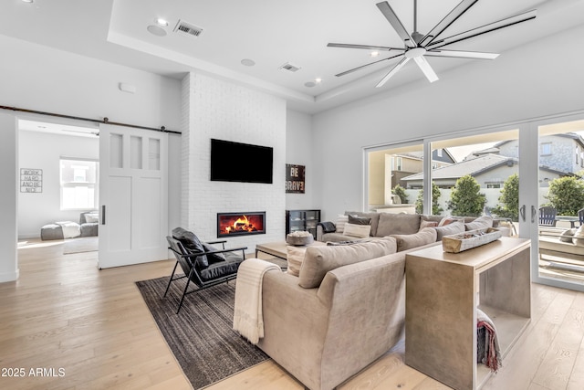 living area with visible vents, light wood-style flooring, a brick fireplace, and a raised ceiling