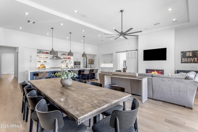 dining space featuring a ceiling fan, visible vents, recessed lighting, light wood-style floors, and a brick fireplace