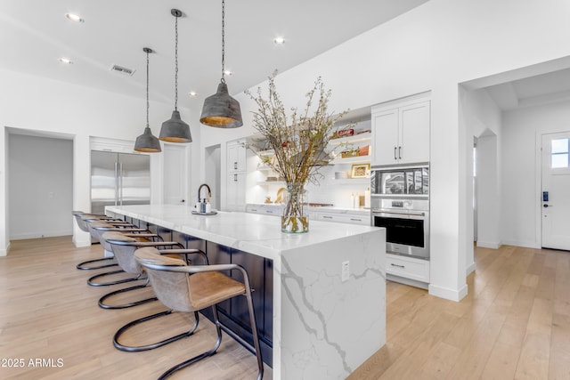 kitchen with light stone counters, light wood-style flooring, built in fridge, white cabinetry, and a kitchen bar