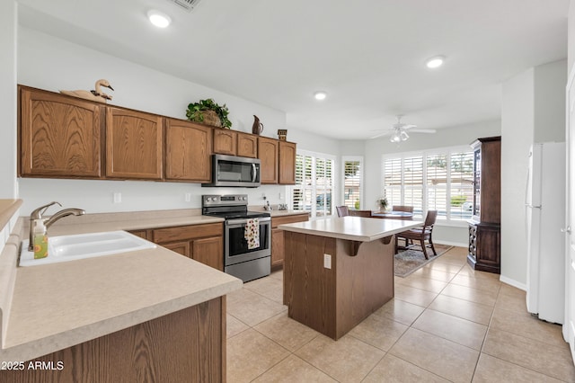 kitchen with a sink, a kitchen island, appliances with stainless steel finishes, light countertops, and light tile patterned floors