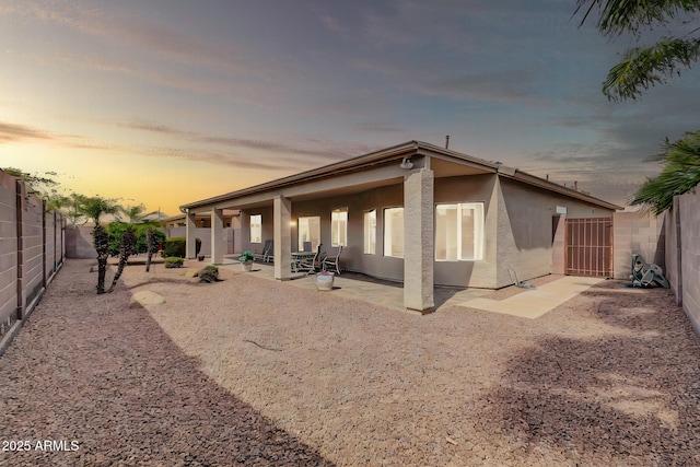 back of property at dusk with stucco siding, a patio, and a fenced backyard