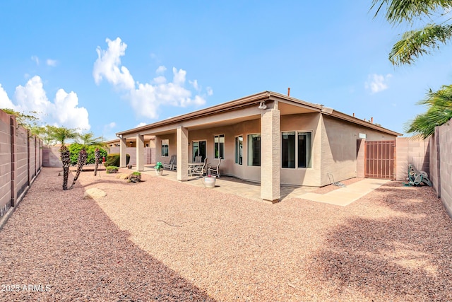 rear view of house with a fenced backyard, stucco siding, a patio, and a gate