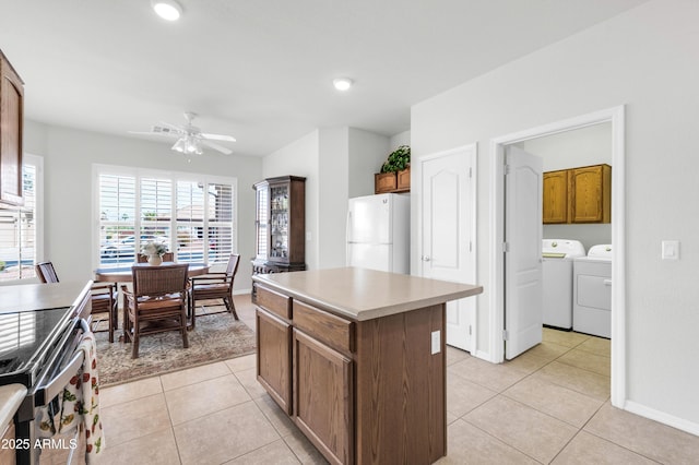 kitchen featuring a center island, ceiling fan, washing machine and dryer, light tile patterned floors, and freestanding refrigerator