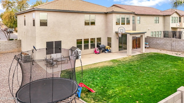 rear view of property with cooling unit, a lawn, a trampoline, and a patio area