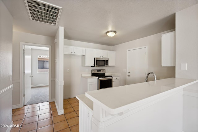 kitchen with a textured ceiling, white cabinetry, kitchen peninsula, appliances with stainless steel finishes, and light tile patterned floors