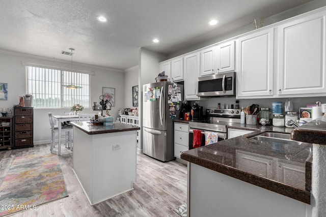 kitchen featuring crown molding, a center island, hanging light fixtures, stainless steel appliances, and white cabinets