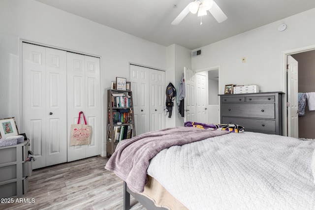 bedroom with two closets, light hardwood / wood-style floors, and ceiling fan