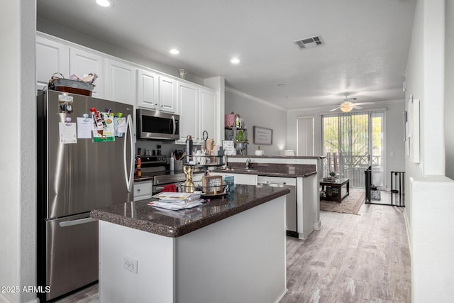 kitchen with light hardwood / wood-style flooring, white cabinetry, stainless steel appliances, a center island, and kitchen peninsula