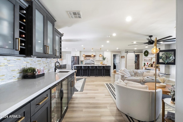 kitchen featuring tasteful backsplash, beverage cooler, sink, a barn door, and light hardwood / wood-style floors