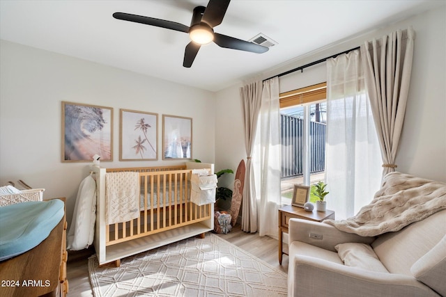 bedroom featuring light wood-type flooring, a nursery area, and ceiling fan