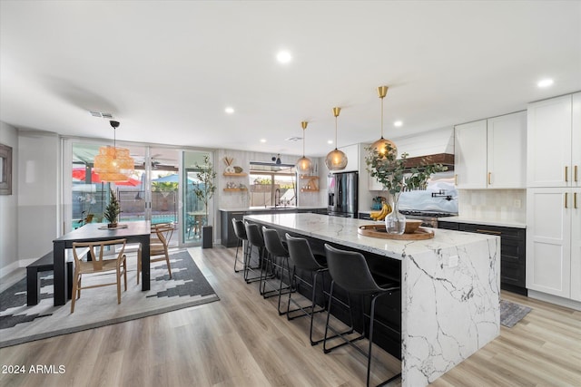 kitchen with pendant lighting, backsplash, white cabinets, light stone countertops, and a large island