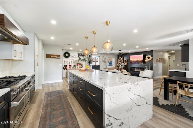 kitchen with pendant lighting, double oven range, premium range hood, light stone countertops, and a fireplace