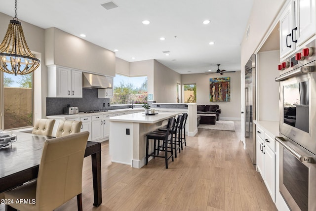 kitchen featuring light hardwood / wood-style floors, pendant lighting, wall chimney range hood, and white cabinets