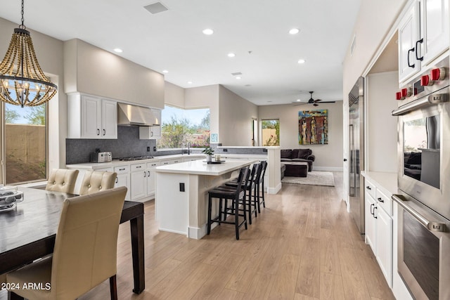 kitchen with decorative backsplash, gas stovetop, wall chimney exhaust hood, light wood-type flooring, and a kitchen breakfast bar