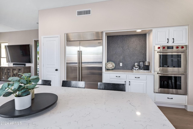 kitchen with stainless steel appliances, hardwood / wood-style floors, white cabinetry, tasteful backsplash, and light stone counters