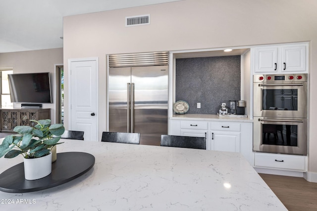 kitchen with stainless steel appliances, visible vents, white cabinets, light stone countertops, and wood finished floors
