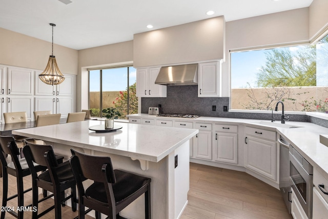 kitchen with decorative backsplash, light hardwood / wood-style floors, pendant lighting, wall chimney range hood, and white cabinets