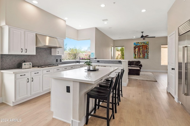 kitchen with a center island, light wood-type flooring, decorative backsplash, ceiling fan, and wall chimney range hood