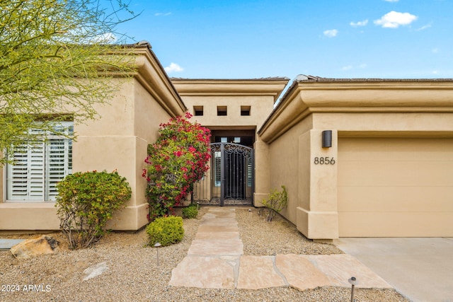 doorway to property featuring a gate, an attached garage, and stucco siding