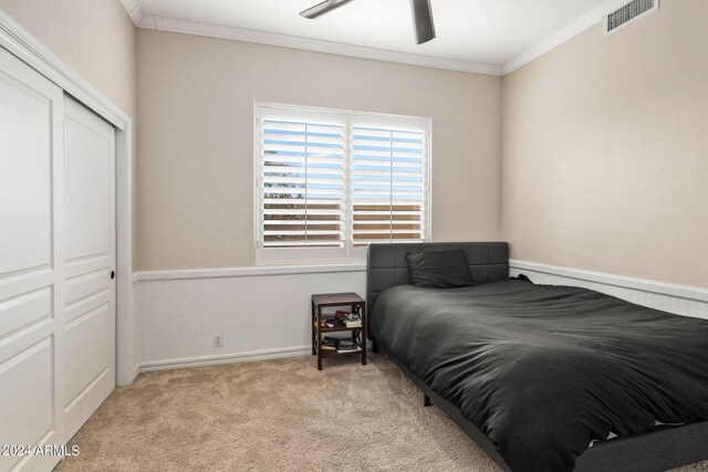 bedroom with crown molding, a closet, a ceiling fan, light colored carpet, and visible vents
