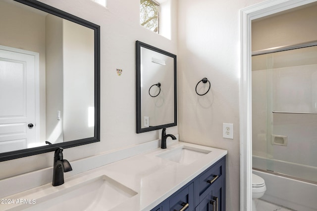 bathroom featuring combined bath / shower with glass door, double vanity, toilet, and a sink