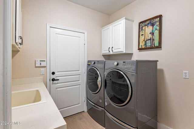 clothes washing area with cabinet space, light wood-style flooring, a sink, and washer and clothes dryer