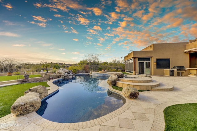 pool at dusk featuring an in ground hot tub, a grill, exterior kitchen, and a patio area