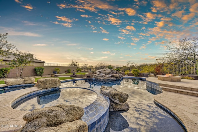 pool at dusk with a fire pit and a patio area