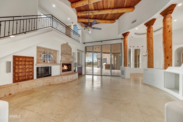 unfurnished living room with wood ceiling, a premium fireplace, ceiling fan, beamed ceiling, and ornate columns